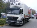 Biały Mercedes Axor z chłodnią, ozdobiony grafiką warzyw, gotowy do dostawy świeżych produktów.
