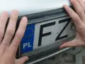 Dłonie trzymają tablicę rejestracyjną z oznaczeniem PL i literami FZ. Może to być związane z czasowe wyrejestrowanie pojazdu.