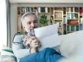 Mężczyzna z siwą brodą czyta dokument, być może wypowiedzenie OC. Na półkach za nim widać książki.