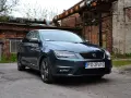 Ciemnoszary Seat przed ceglanym budynkiem z rdzawymi rurami.