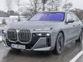 Szary BMW M7 pędzi po mokrej drodze, otoczony zimowym krajobrazem.