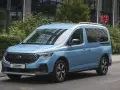 Niebieski Ford Tourneo Connect zaparkowany na ulicy, z budynkiem i zielenią w tle.