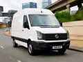 Biały Volkswagen Crafter 2.5 TDI w ruchu miejskim, z widocznymi budynkami w tle.
