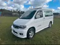 Biały van Mazda Bongo z podnoszonym dachem, zaparkowany na trawie.
