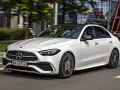Biały Mercedes C 200 z czarnym dachem sunie po miejskiej drodze, odbijając światła budynków w szybach.