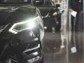 Błyszczący, ciemny samochód na raty z włączonymi światłami. W tle widać drugie auto i sylwetkę klienta.