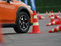 Pomarańczowy samochód na placu manewrowym, otoczony pachołkami. Zastanawiasz się, ile kosztuje prawo jazdy?