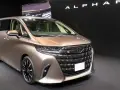 Brązowy minivan Toyota Alphard na ciemnym tle, z widocznym napisem "ALPHARD".