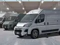 Rząd szarych furgonetek Fiat Ducato Maxi w magazynie z półkami i pudełkami.