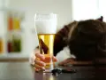Ręka trzymająca piwo, obok kluczyki samochodowe. Osoba w tle pochylona.