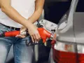 Kobieta tankuje samochód, nalewając paliwo. W tle widać fragment auta i dystrybutor. Może to być paliwo verva 98.