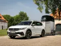 Biały Volkswagen SUV z przyczepą do przewozu koni stoi przed starym budynkiem.