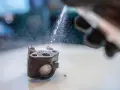 Ręka w rękawicy rozpyla wodę na zardzewiały element, być może zawór EGR, który jest czyszczony.