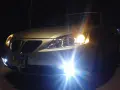 Srebrny samochód nocą, włączone światła przeciwmgielne i mijania rozświetlają drogę.