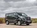 Ciemnoszary van Renault z przyciemnianymi szybami stoi na tle chmur i krzaków.
