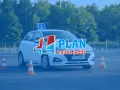 Biały samochód z literą "L" na dachu i pachołkami na placu manewrowym. To idealne miejsce na praktyczny egzamin na prawo jazdy.