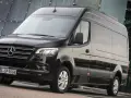 Czarny furgon Mercedes-Benz Sprinter stoi przed nowoczesnym budynkiem z przeszkloną fasadą.