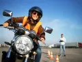 Uśmiechnięta kursantka na motocyklu, gotowa do egzaminu na prawo jazdy kat. A. Sprawdza cenę kursu.