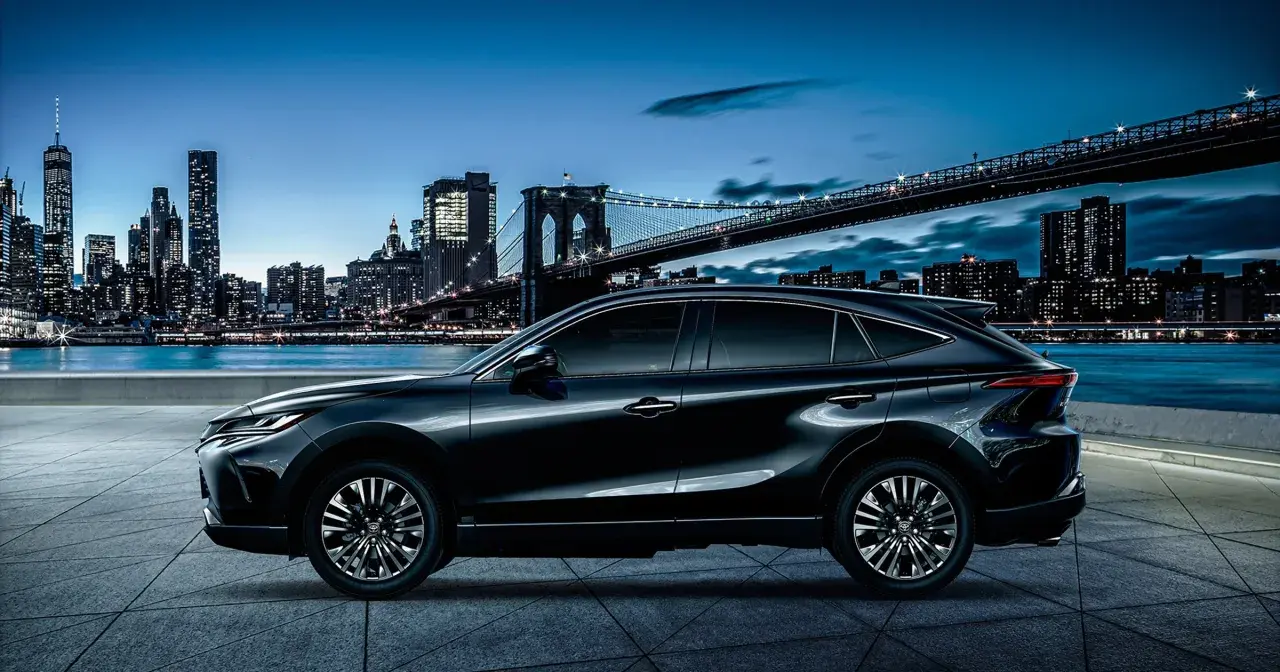 Elegancki, czarny Toyota Harrier lśni nocą na tle rozświetlonego miasta i mostu.