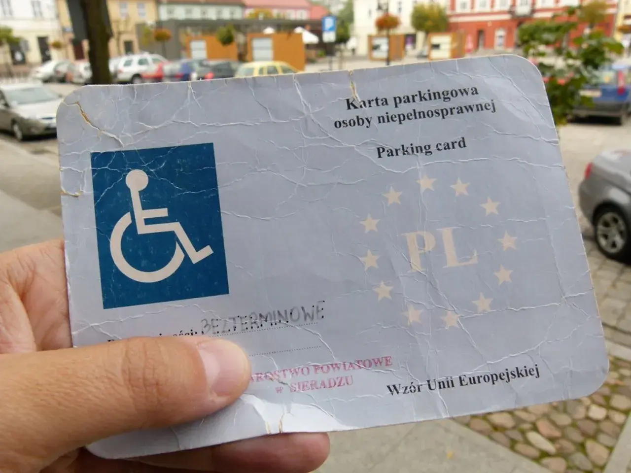 Karta parkingowa dla niepełnosprawnych, z symbolem wózka inwalidzkiego i gwiazdkami UE. Ułatwia parkowanie w mieście.