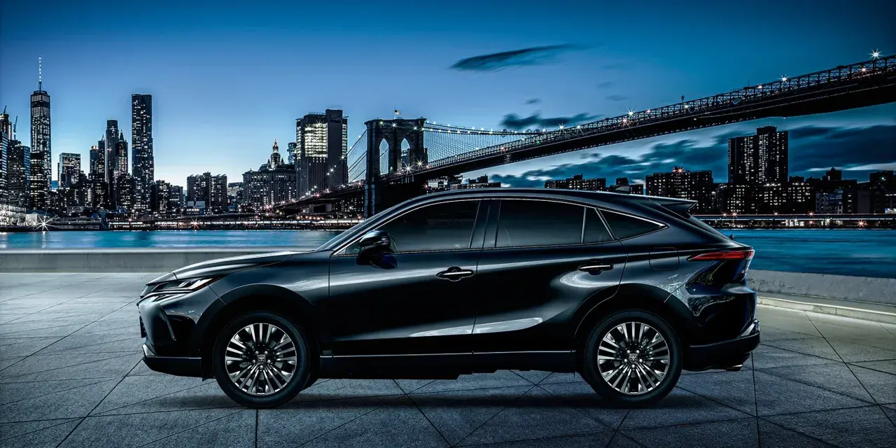 Elegancki, czarny Toyota Harrier lśni nocą na tle rozświetlonego miasta i mostu.