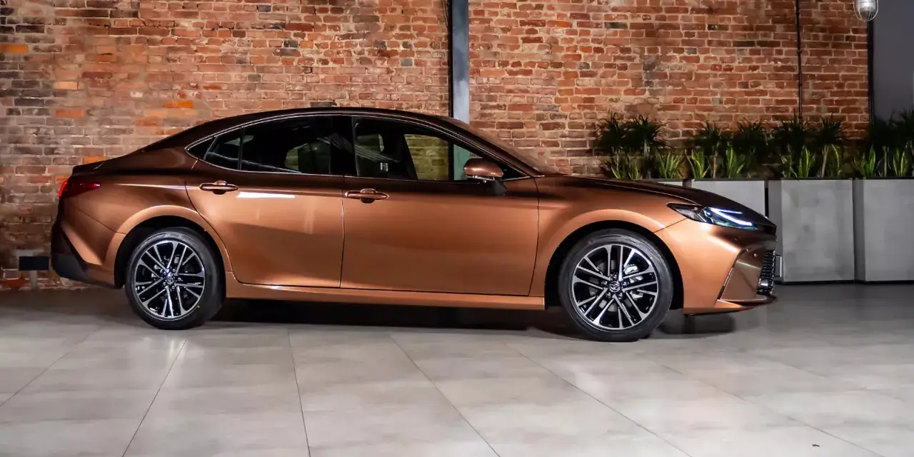 Elegancki, brązowy sedan auto z nowoczesnymi felgami stoi na tle ceglanej ściany.
