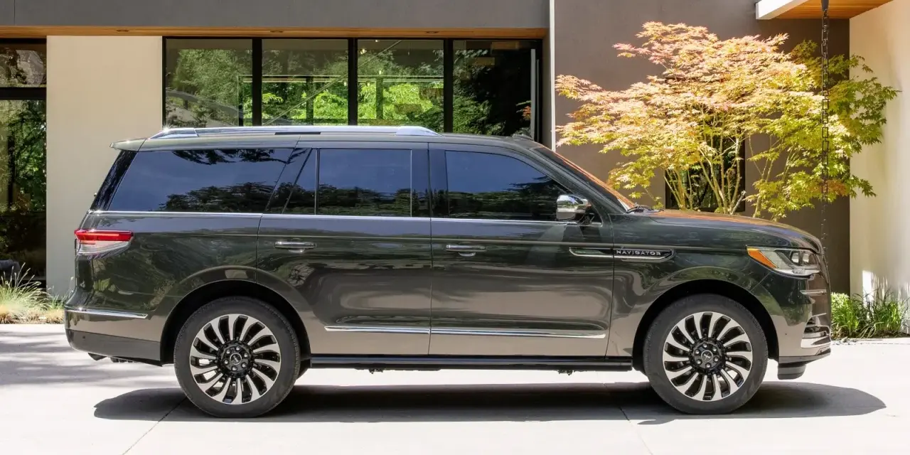 Ciemnoszary Lincoln Navigator SUV zaparkowany przed nowoczesnym domem z drzewem klonu japońskiego.