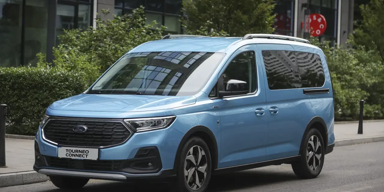 Niebieski Ford Tourneo Connect zaparkowany na ulicy, z budynkiem i zielenią w tle.