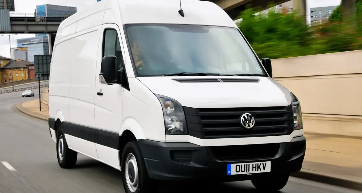Biały Volkswagen Crafter 2.5 TDI w ruchu miejskim, z widocznymi budynkami w tle.