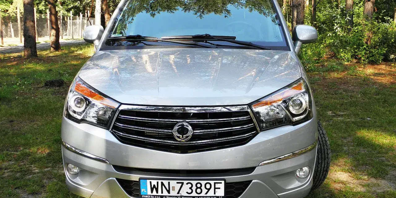Srebrny SsangYong Rodius z przodu, zaparkowany na tle lasu.