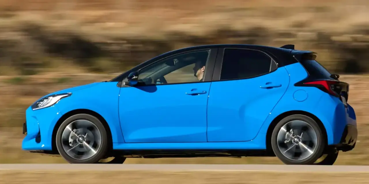 Niebieski hatchback z czarnym dachem pędzi po drodze, za kierownicą siedzi mężczyzna.