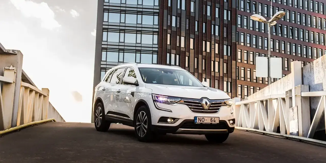 Biały Renault Koleos na tle nowoczesnego budynku. Czy warto zainwestować? Sprawdź interrisk opinie.