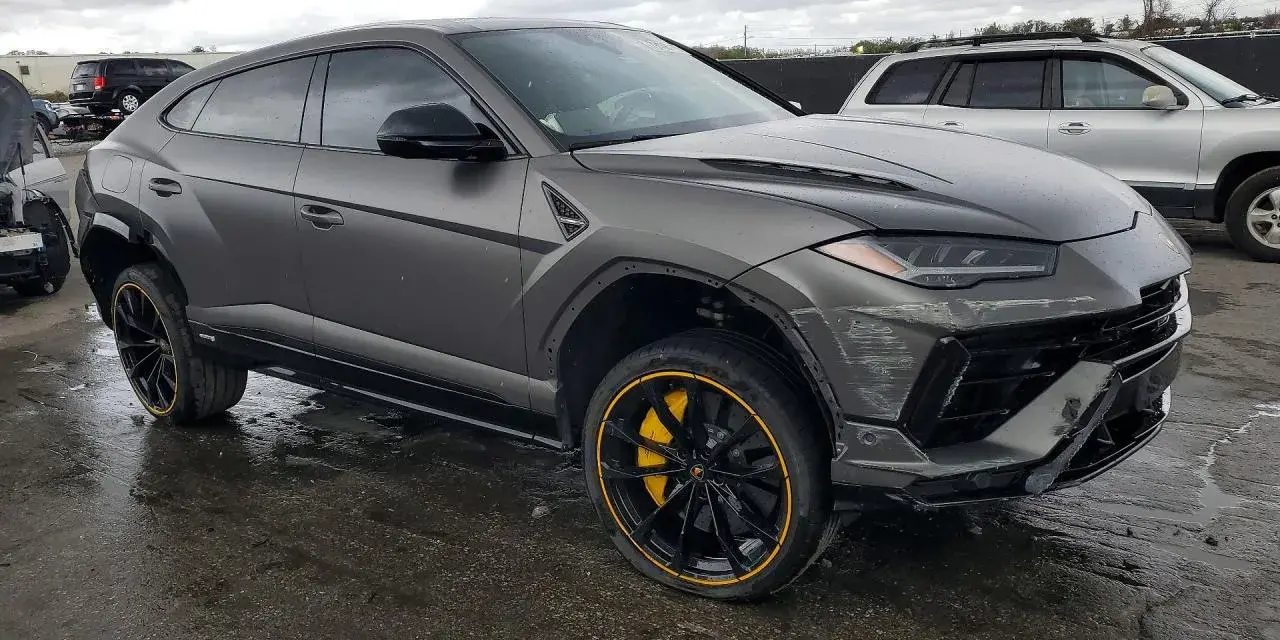 Szary Lamborghini Urus z żółtymi akcentami na felgach, uszkodzony z przodu. Zastanawiasz się nad lamborghini urus cena?