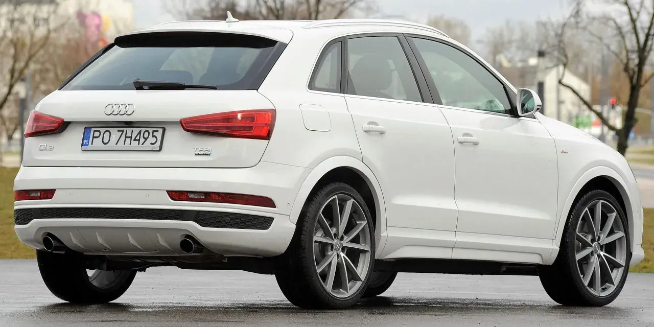 Biały SUV Audi Q3, idealny suv do 70 tys. zł, z polskimi tablicami rejestracyjnymi PO 7H495, widoczny z tyłu i z boku.