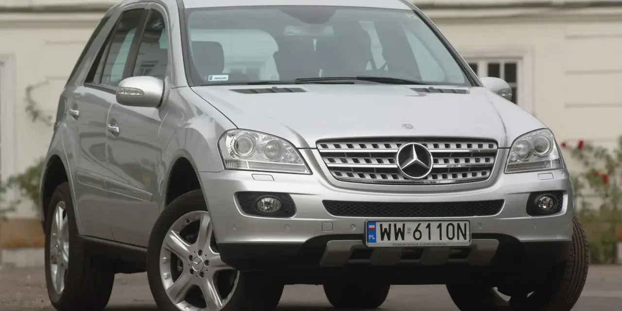 Srebrny Mercedes ML 320 z polskimi tablicami rejestracyjnymi WW 6110N zaparkowany przed budynkiem.
