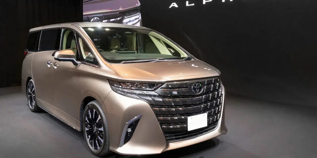 Brązowy minivan Toyota Alphard na ciemnym tle, z widocznym napisem "ALPHARD".