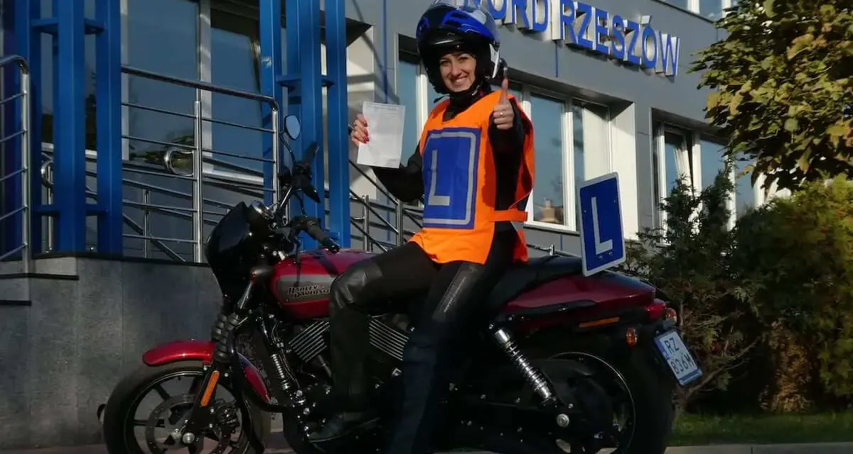 Szczęśliwa kursantka z prawem jazdy kat. A na motocyklu, w kamizelce z literą L, przed budynkiem WORD.