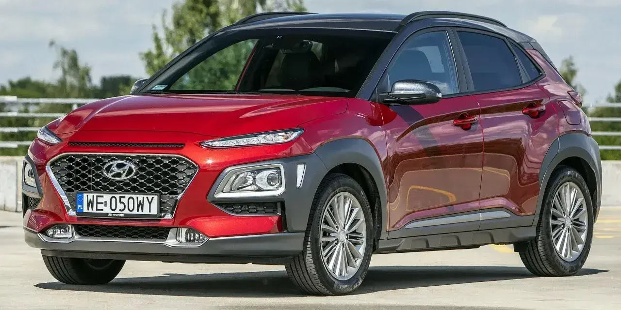 Czerwony, mały SUV Hyundai Kona z czarnym dachem, zaparkowany na zewnątrz.