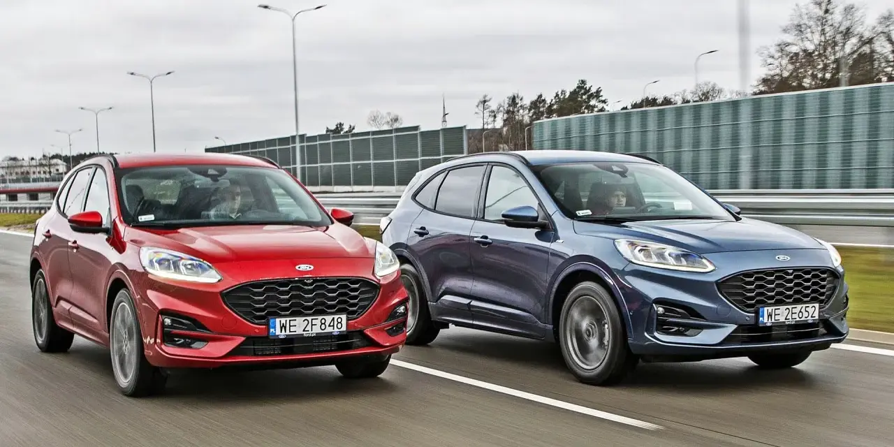 Dwa Fordy SUV, czerwony i granatowy, jadące obok siebie po drodze.