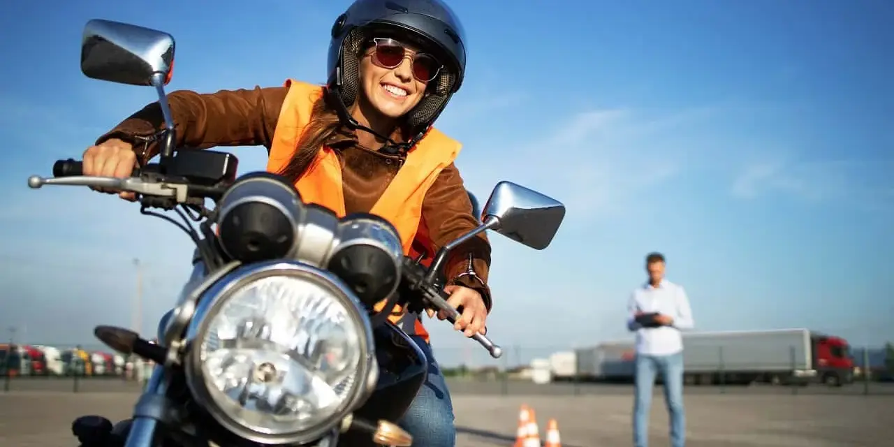 Uśmiechnięta kursantka na motocyklu, gotowa do egzaminu na prawo jazdy kat. A. Sprawdza cenę kursu.