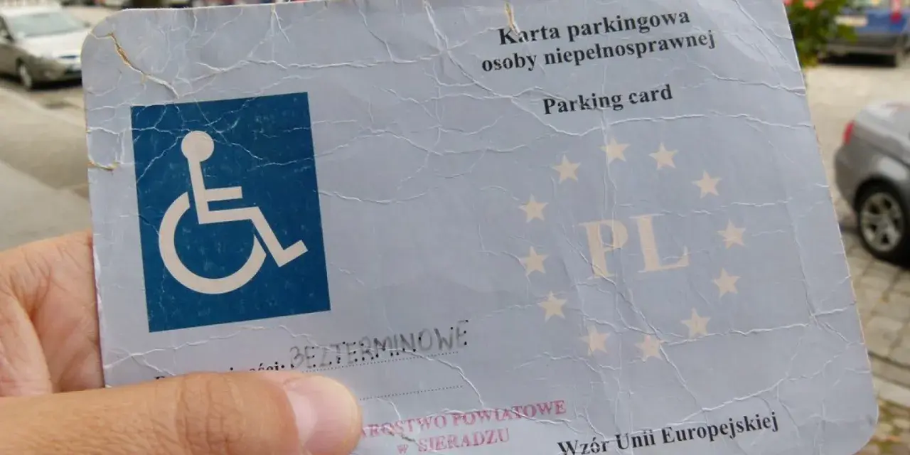 Karta parkingowa dla niepełnosprawnych, z symbolem wózka inwalidzkiego i gwiazdkami UE. Ułatwia parkowanie w mieście.