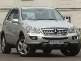 Srebrny Mercedes ML 320 z polskimi tablicami rejestracyjnymi WW 6110N zaparkowany przed budynkiem.