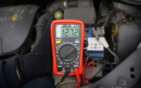 Multimetr pokazuje 12.72V, co oznacza prawidłowe napięcie akumulatora. Sprawdzanie stanu baterii przed podróżą.