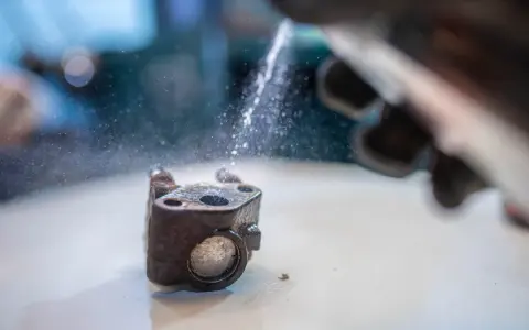 Ręka w rękawicy rozpyla wodę na zardzewiały element, być może zawór EGR, który jest czyszczony.