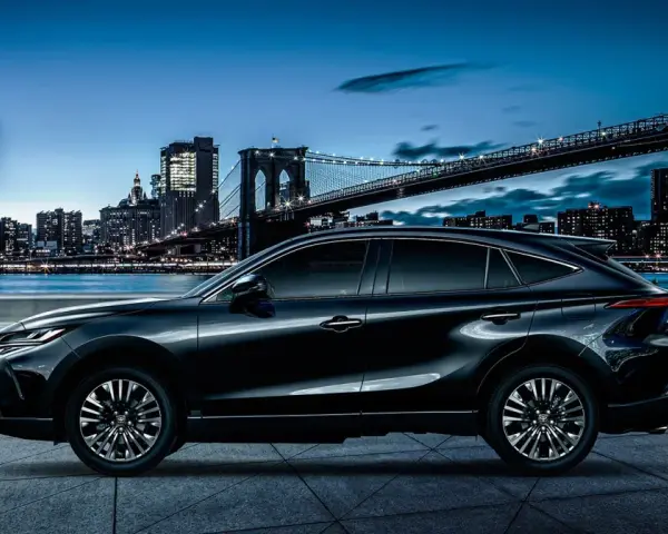 Elegancki, czarny Toyota Harrier lśni nocą na tle rozświetlonego miasta i mostu.
