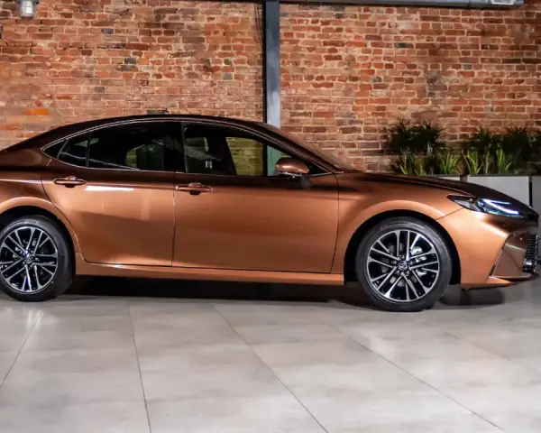 Elegancki, brązowy sedan auto z nowoczesnymi felgami stoi na tle ceglanej ściany.