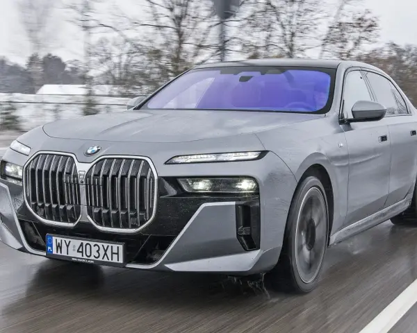 Szary BMW M7 pędzi po mokrej drodze, otoczony zimowym krajobrazem.