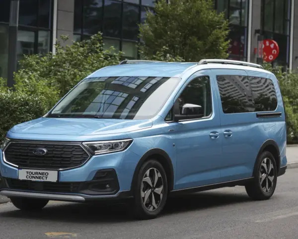 Niebieski Ford Tourneo Connect zaparkowany na ulicy, z budynkiem i zielenią w tle.