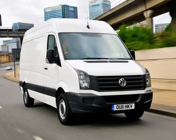 Biały Volkswagen Crafter 2.5 TDI w ruchu miejskim, z widocznymi budynkami w tle.