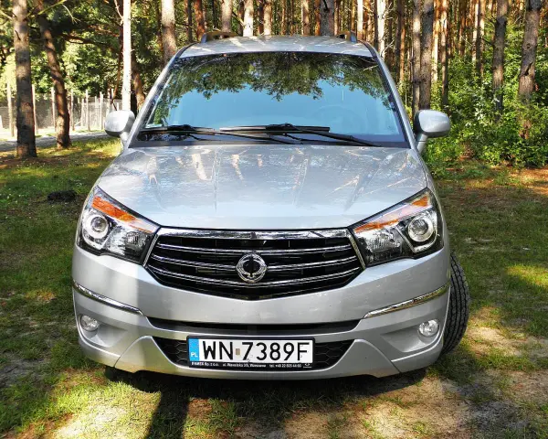 Srebrny SsangYong Rodius z przodu, zaparkowany na tle lasu.